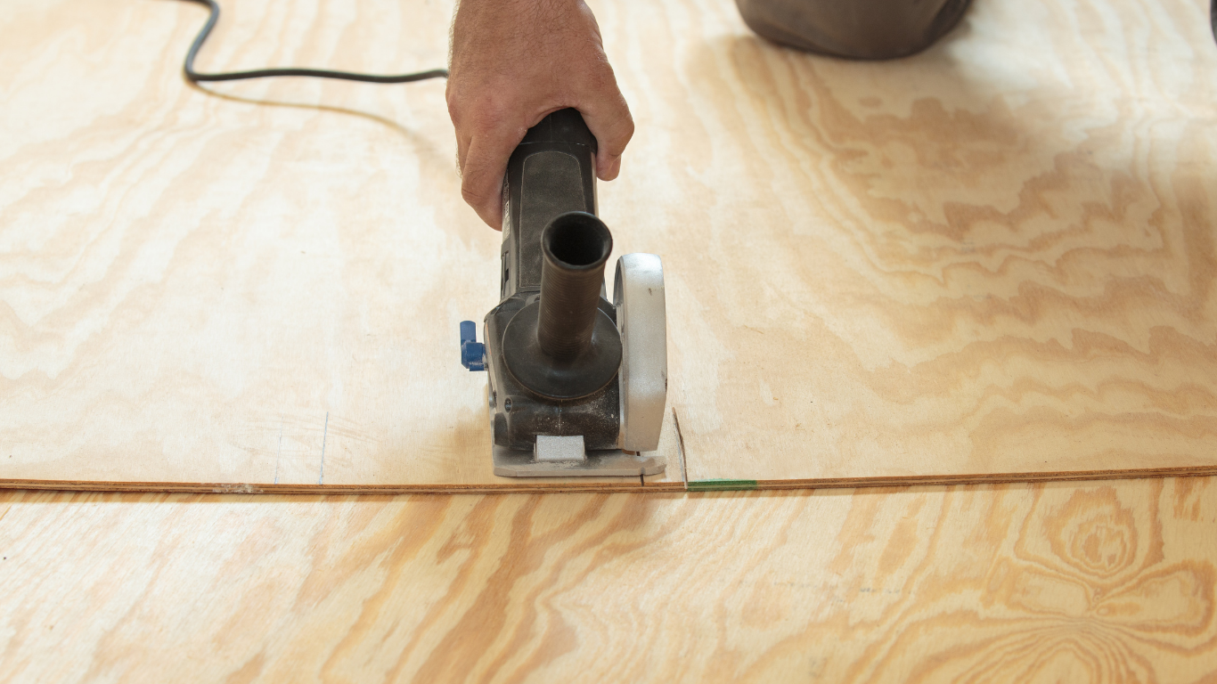 A person using a circular saw to cut a piece of plywood.