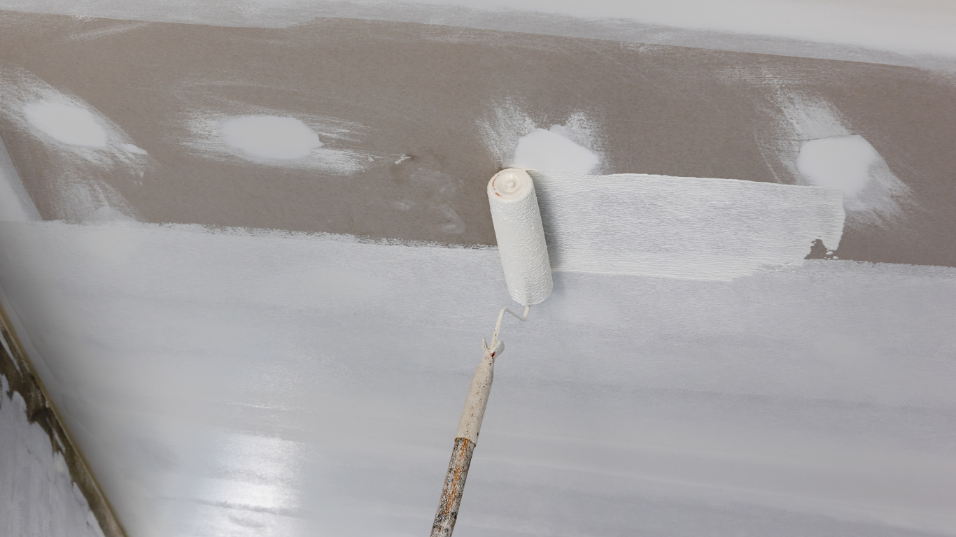 A person paints a ceiling white with a roller, covering patched areas.