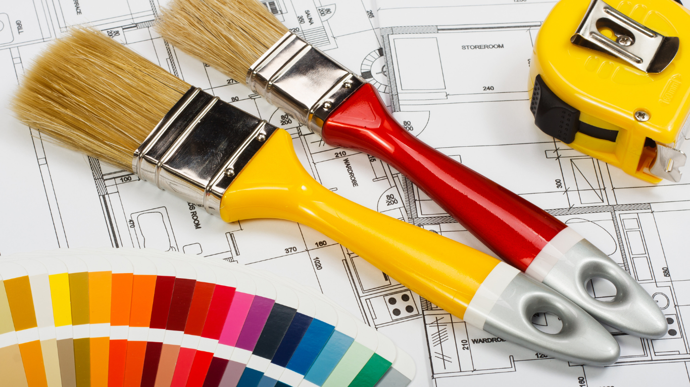 Two paint brushes on blueprints with a color swatch and tape measure.