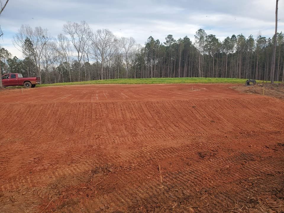 A red truck is parked in the middle of a dirt field.