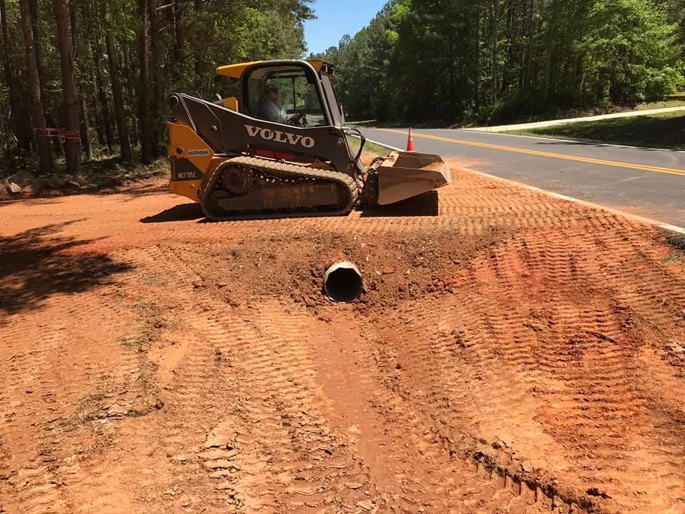 A volvo bulldozer is working on a dirt road next to a road.
