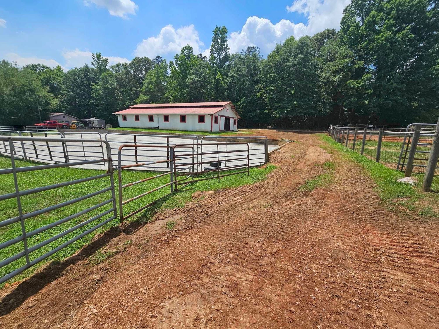 A dirt road leading to a white building with a red roof