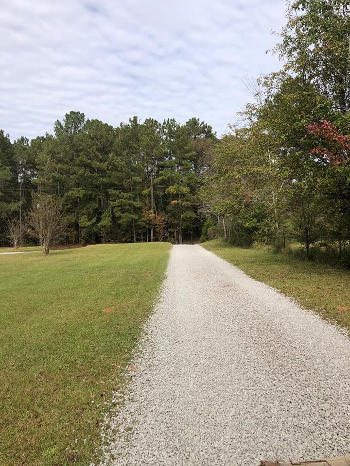 A gravel road going through a grassy field with trees on both sides.