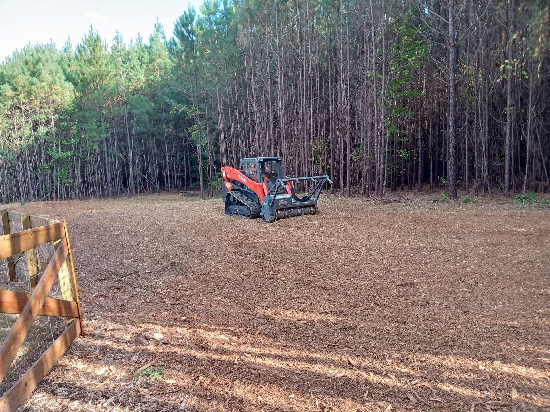 A bulldozer is driving through a dirt field in the middle of a forest.
