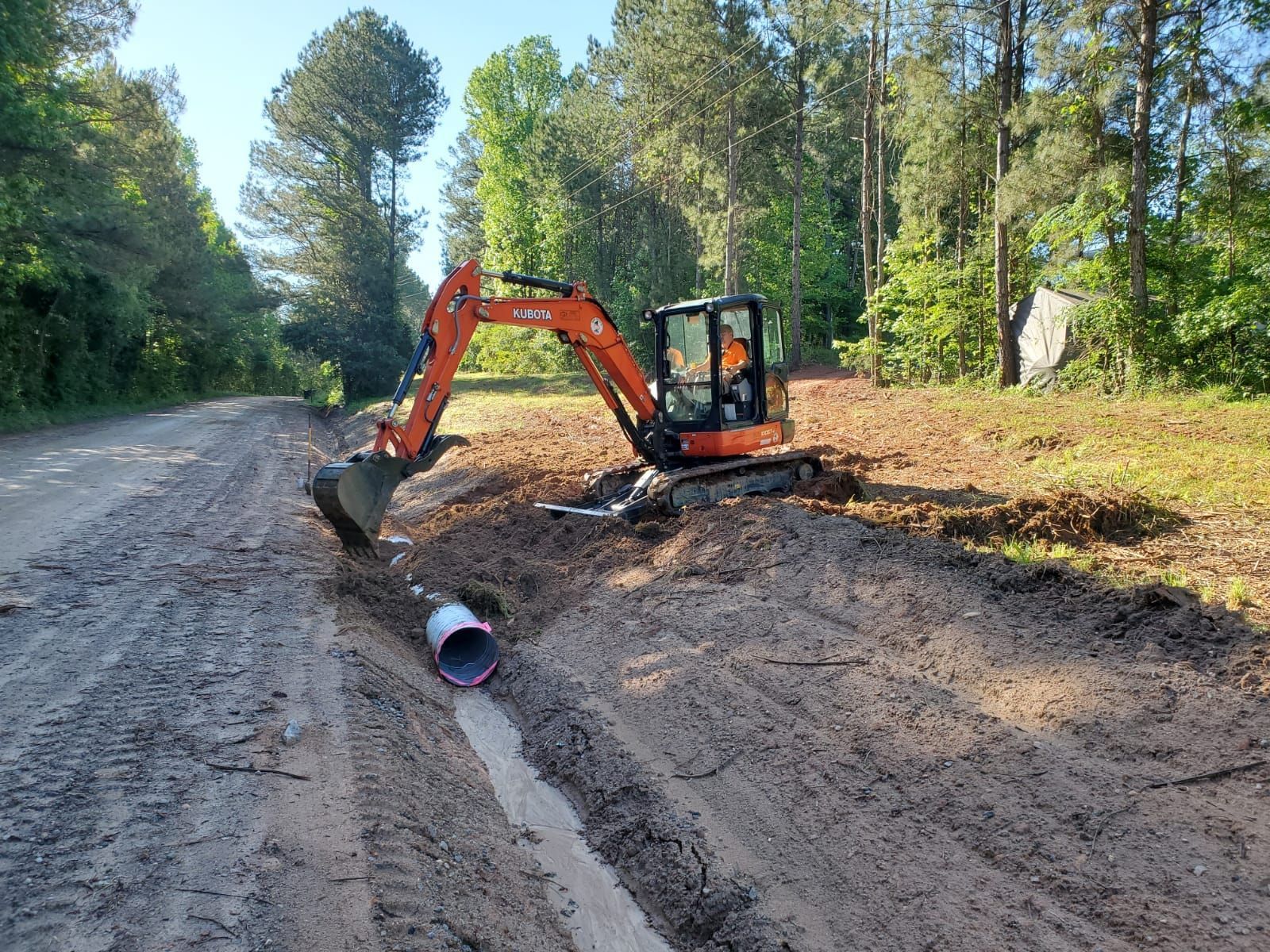 An excavator is digging a hole in the dirt next to a road.