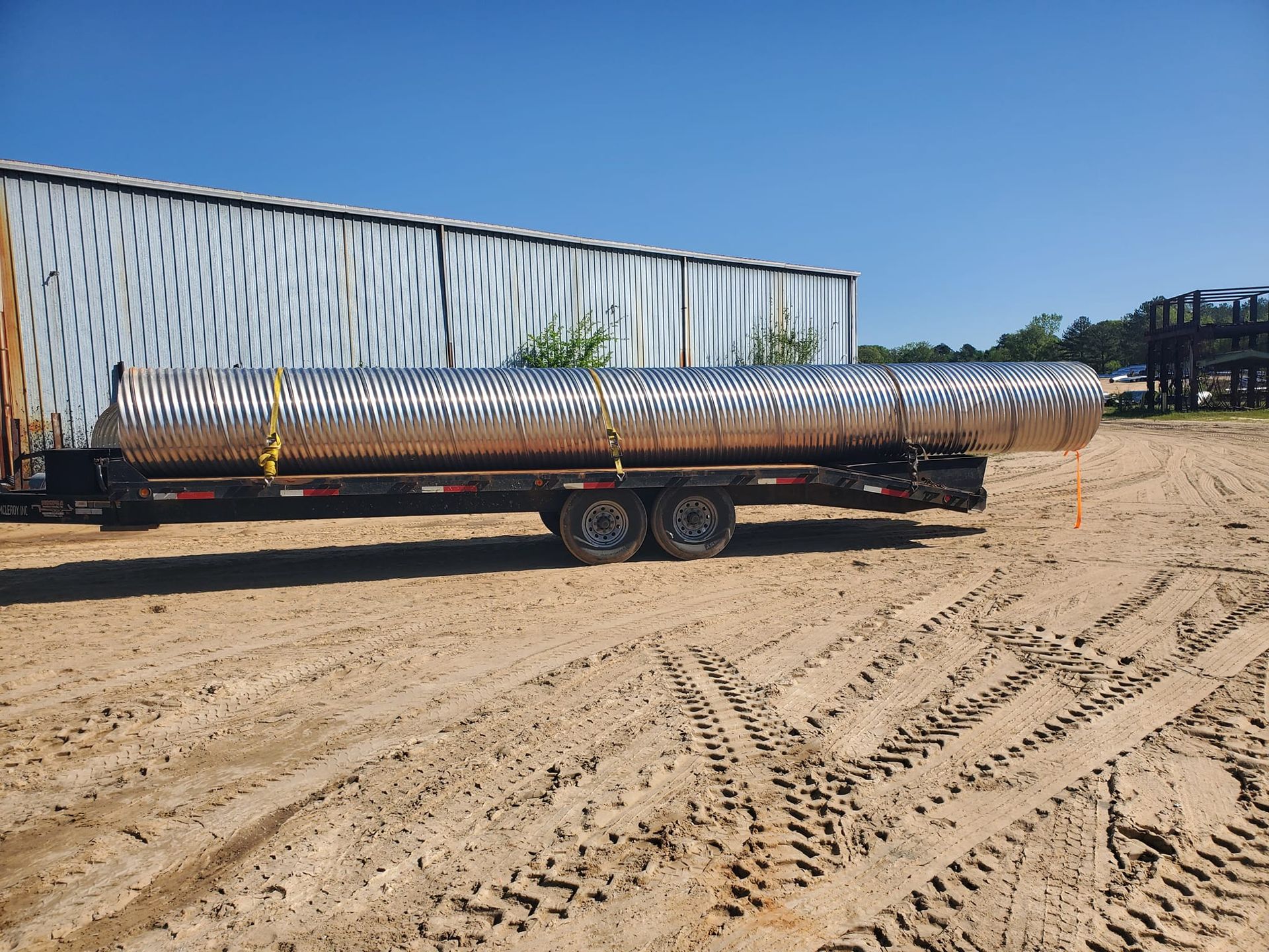 A large metal pipe is sitting on top of a trailer in a dirt field.