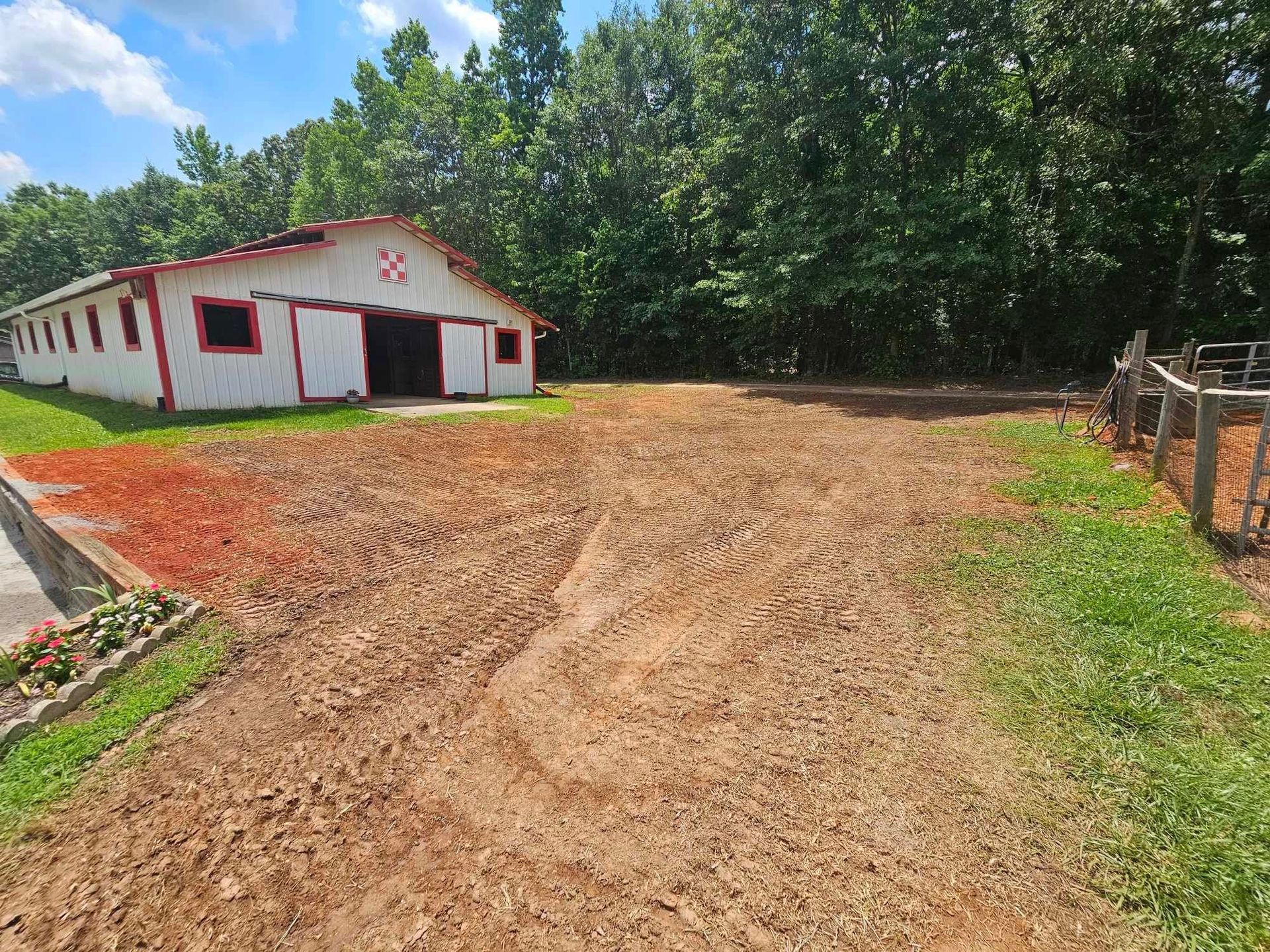 A white barn with red trim is sitting on top of a dirt field.