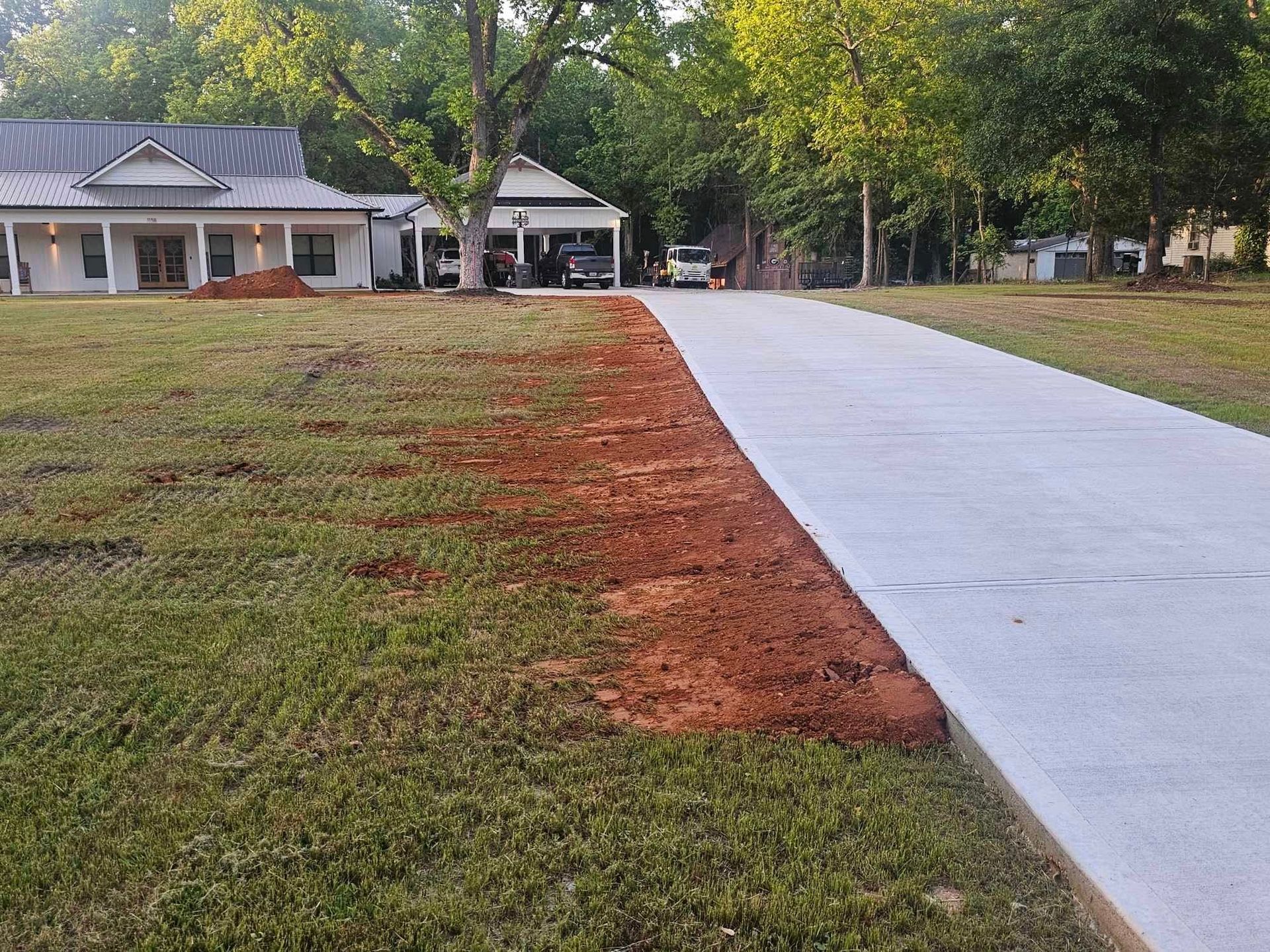 A concrete driveway leading to a house in the middle of a grassy field.