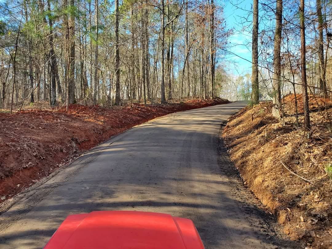 A red car is driving down a dirt road in the woods.