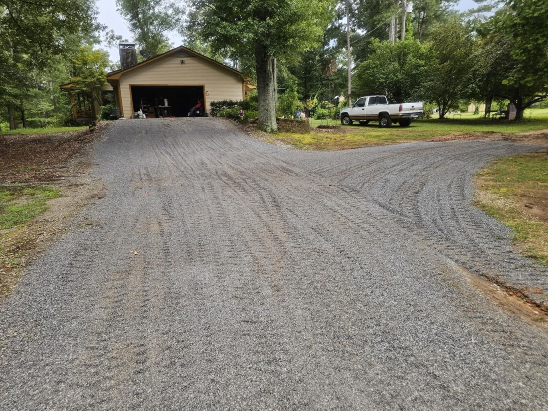 A gravel driveway leading to a house with a truck parked in front of it.
