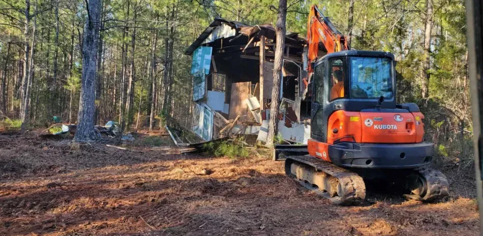 An excavator is demolishing a house in the woods.