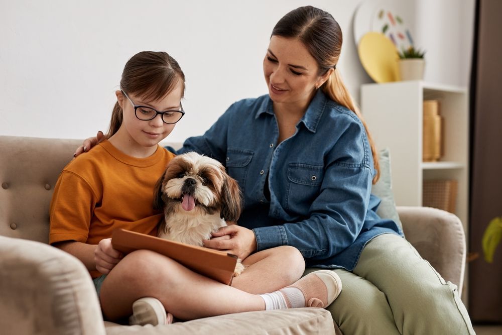 Mother and daughter playing with a dog on the couch at home - First Aid in Mackay, QLD