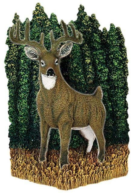 A deer is standing in a field in front of a forest.