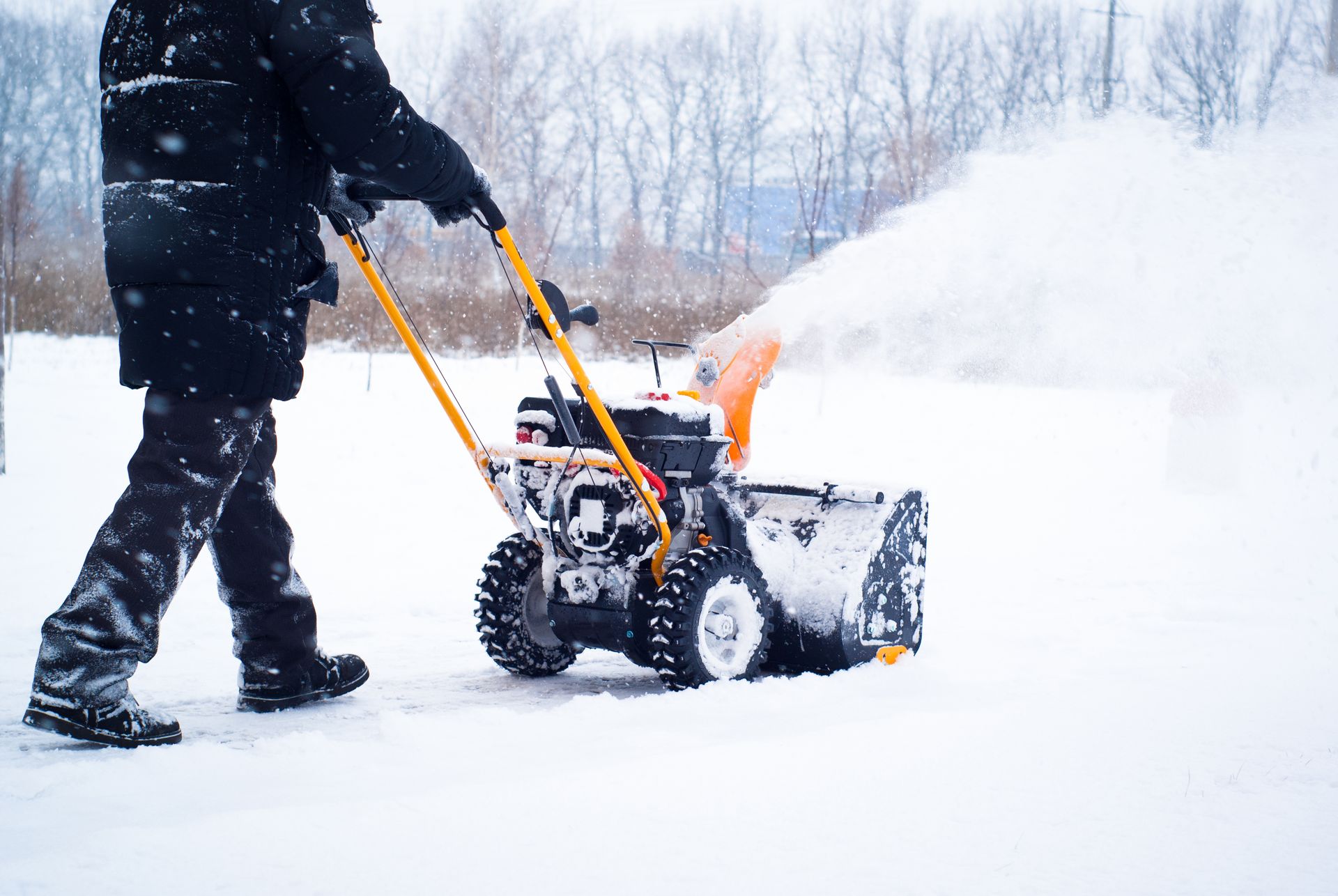 Person using a yellow snowblower to clear snow in a snowy, outdoor setting.