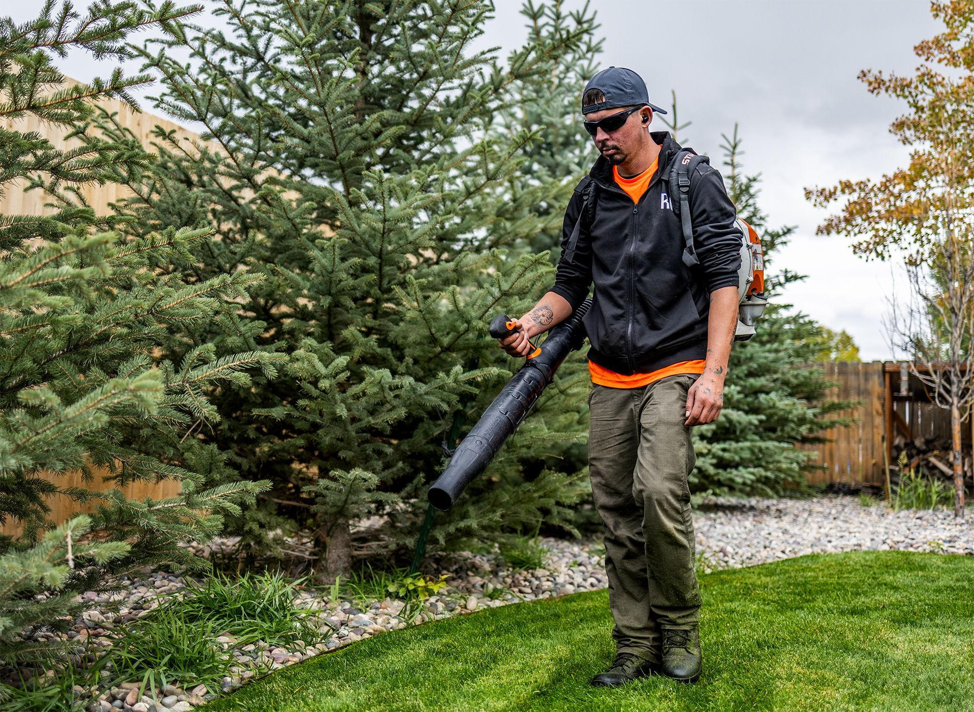 Man using a leaf blower on a lawn with trees in the background.