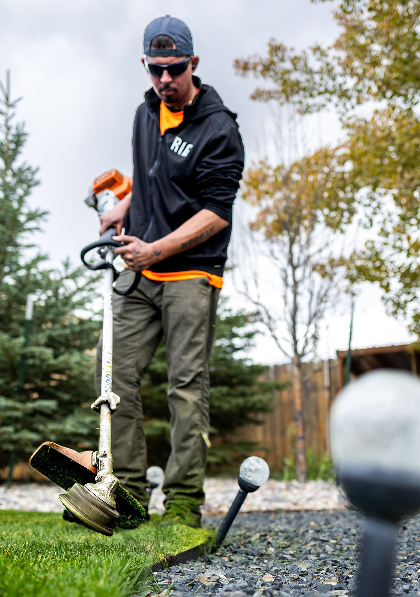Man using a weed whacker to trim grass near a paved edge, outdoors.