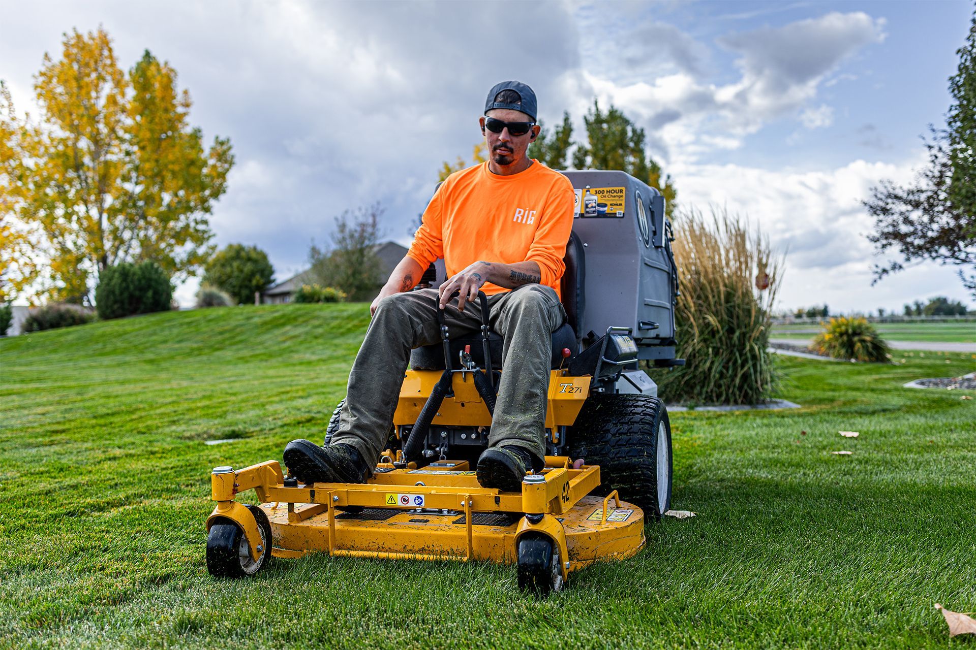 Man on yellow riding lawnmower in a grassy field on a cloudy day.