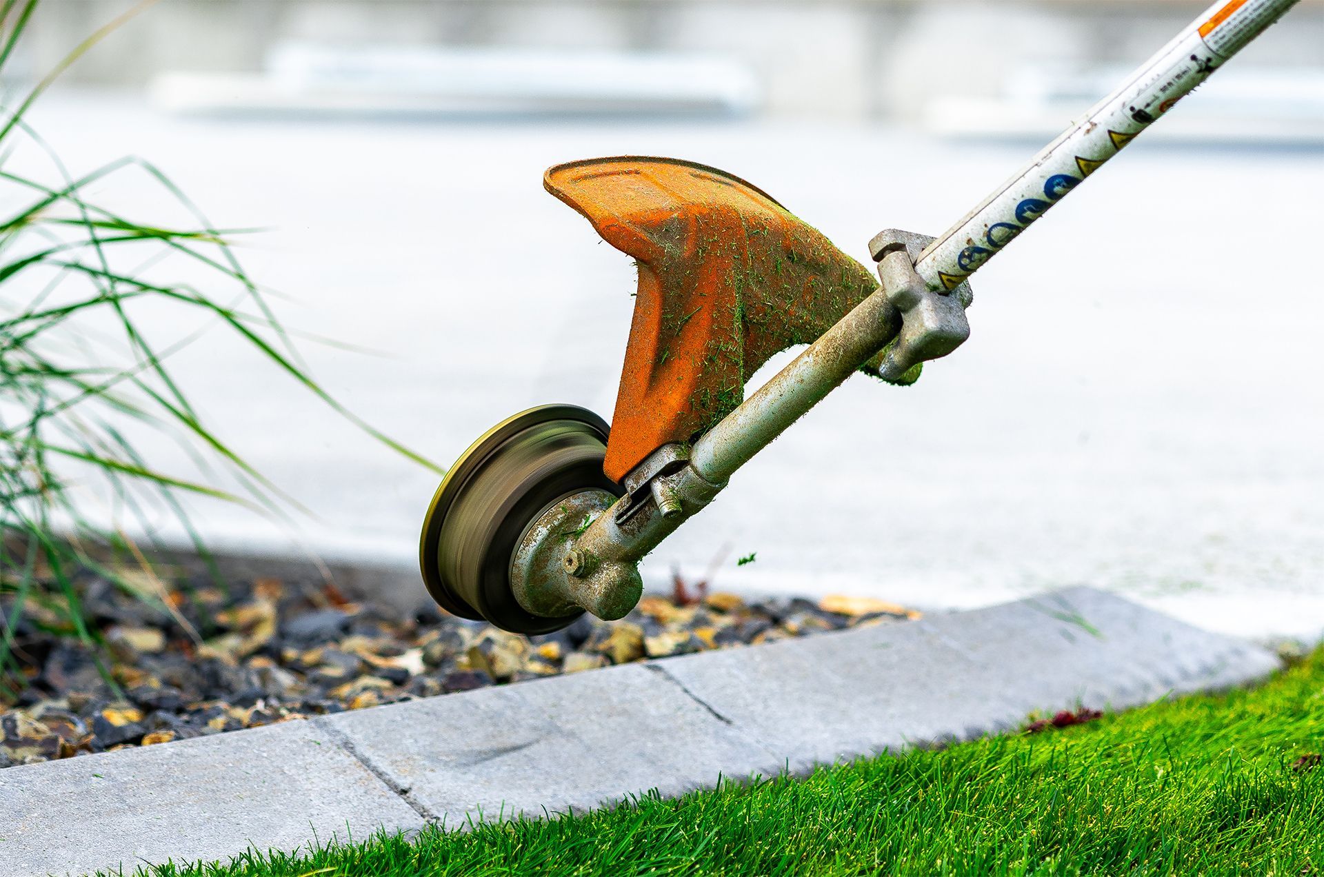 String trimmer edging a lawn near a concrete border, with a parking lot visible in the background.