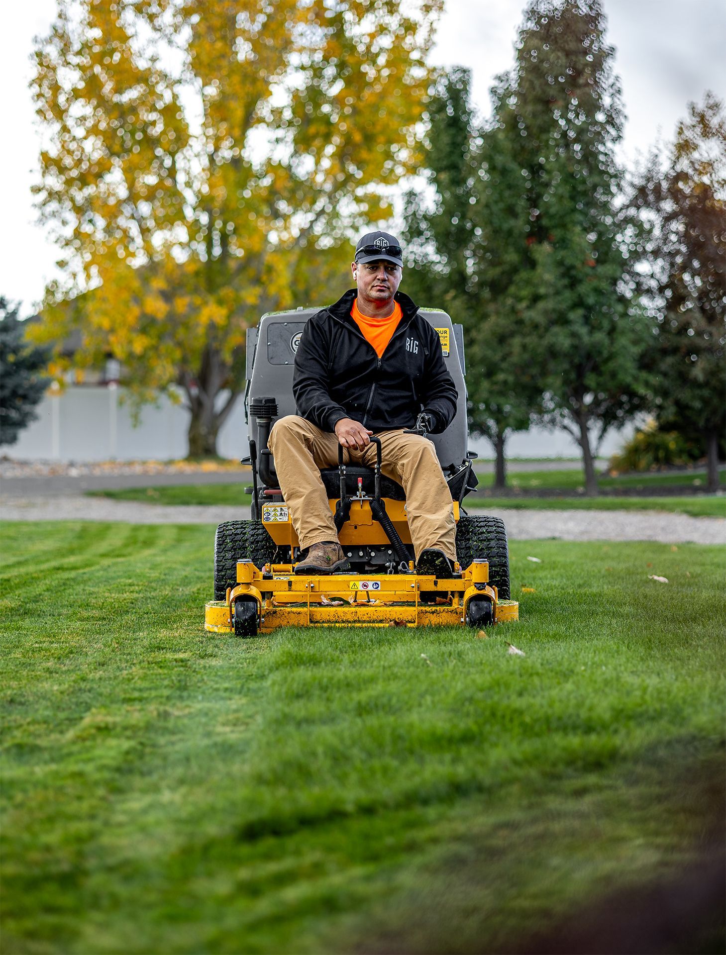 Man on yellow riding lawn mower cutting grass in front of trees.