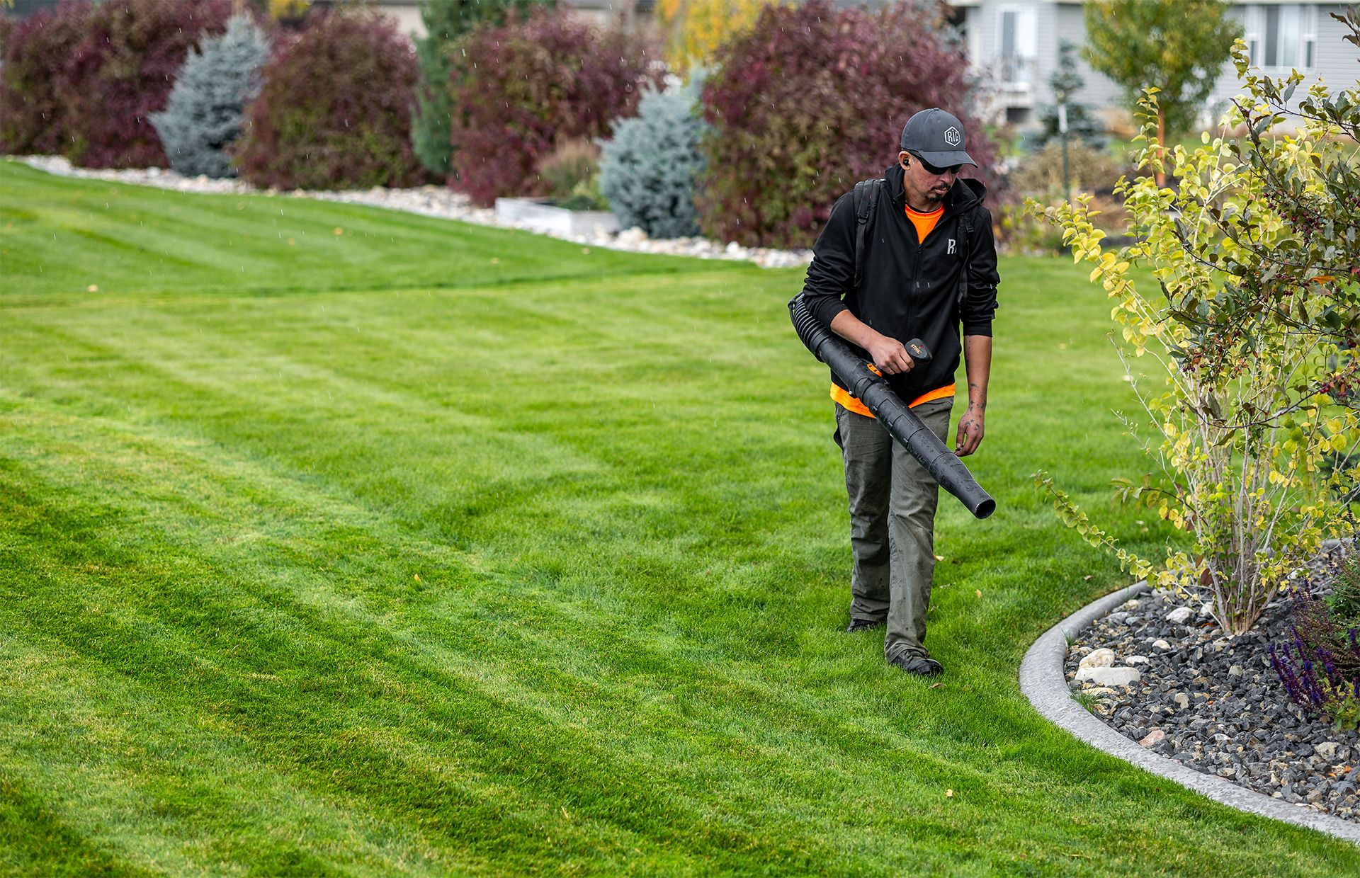 Man using leaf blower on a well-manicured lawn with green grass and neatly trimmed edges.