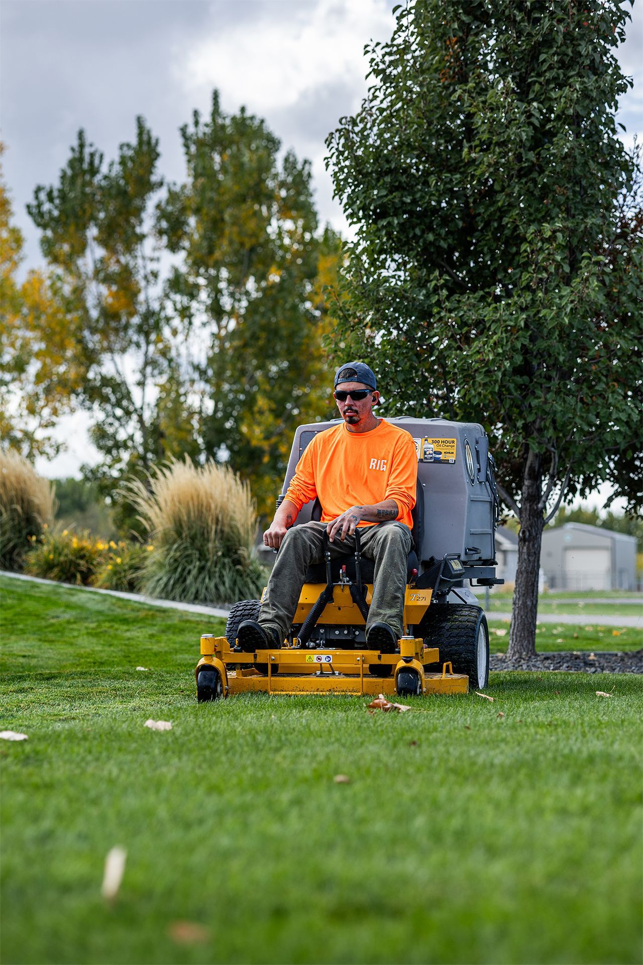 A person in an orange shirt operating a yellow zero-turn lawn mower on a grassy lawn.