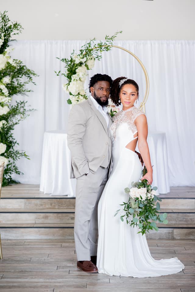 A bride and groom are posing for a picture in front of a floral arch.