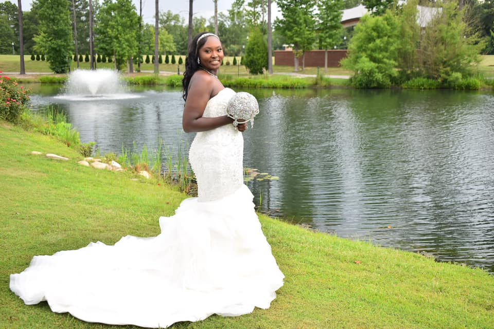 A woman in a wedding dress is standing in front of a lake holding a bouquet of flowers.