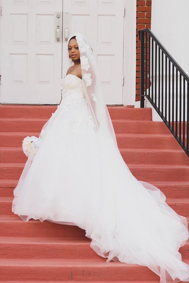 A bride in a wedding dress and veil is walking down red stairs.