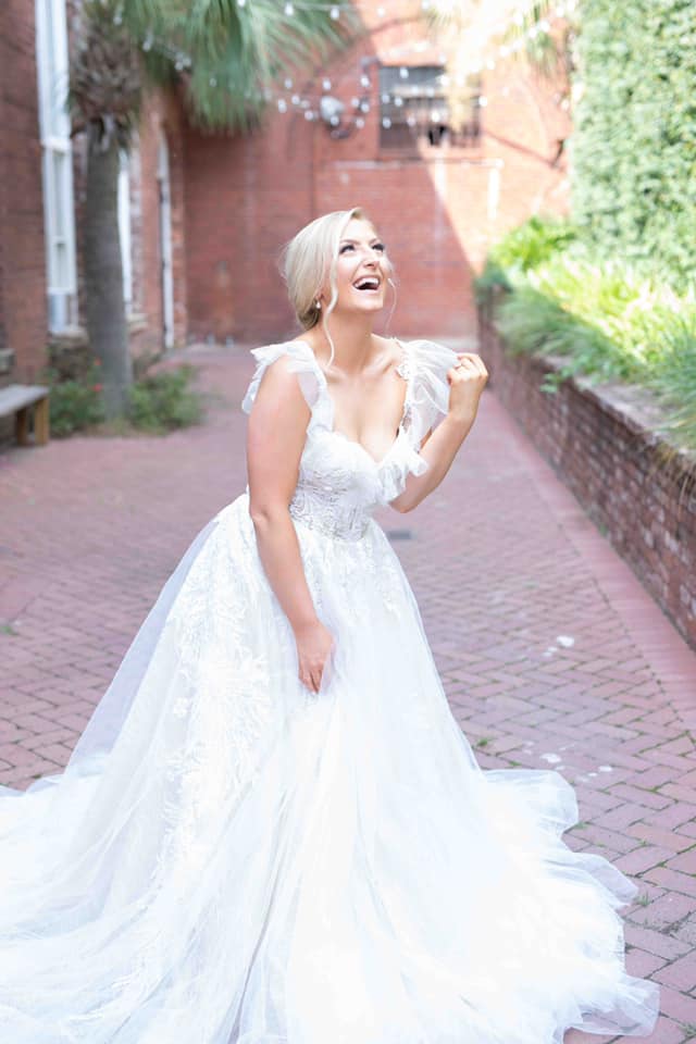 A woman in a wedding dress is standing on a brick sidewalk.
