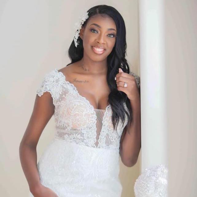 A woman in a wedding dress is leaning against a wall.