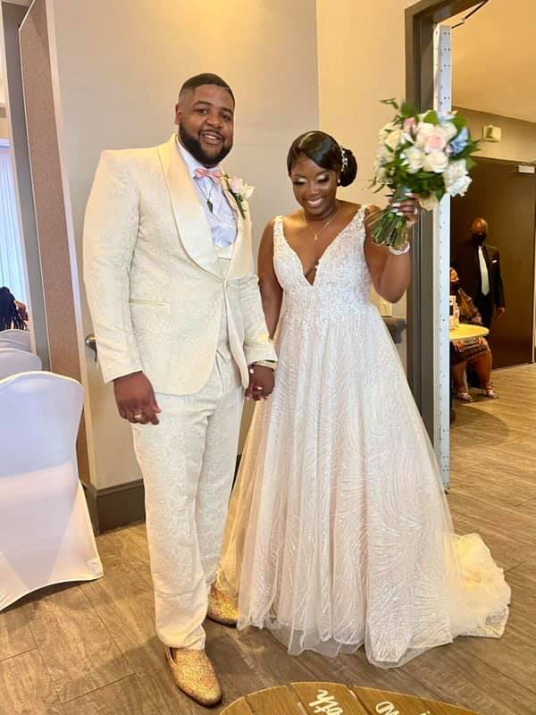 A bride and groom are standing next to each other in a room holding hands.