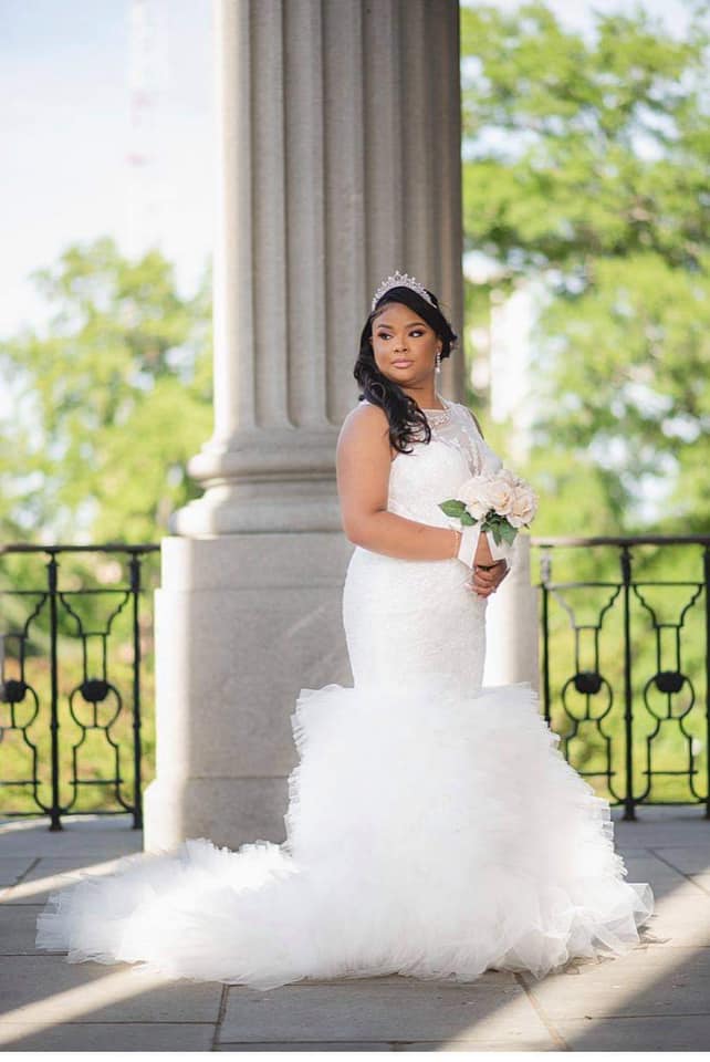 A woman in a wedding dress is standing in front of a pillar holding a bouquet of flowers.