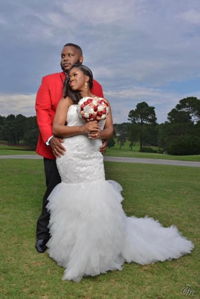 A bride and groom are posing for a picture in the grass.