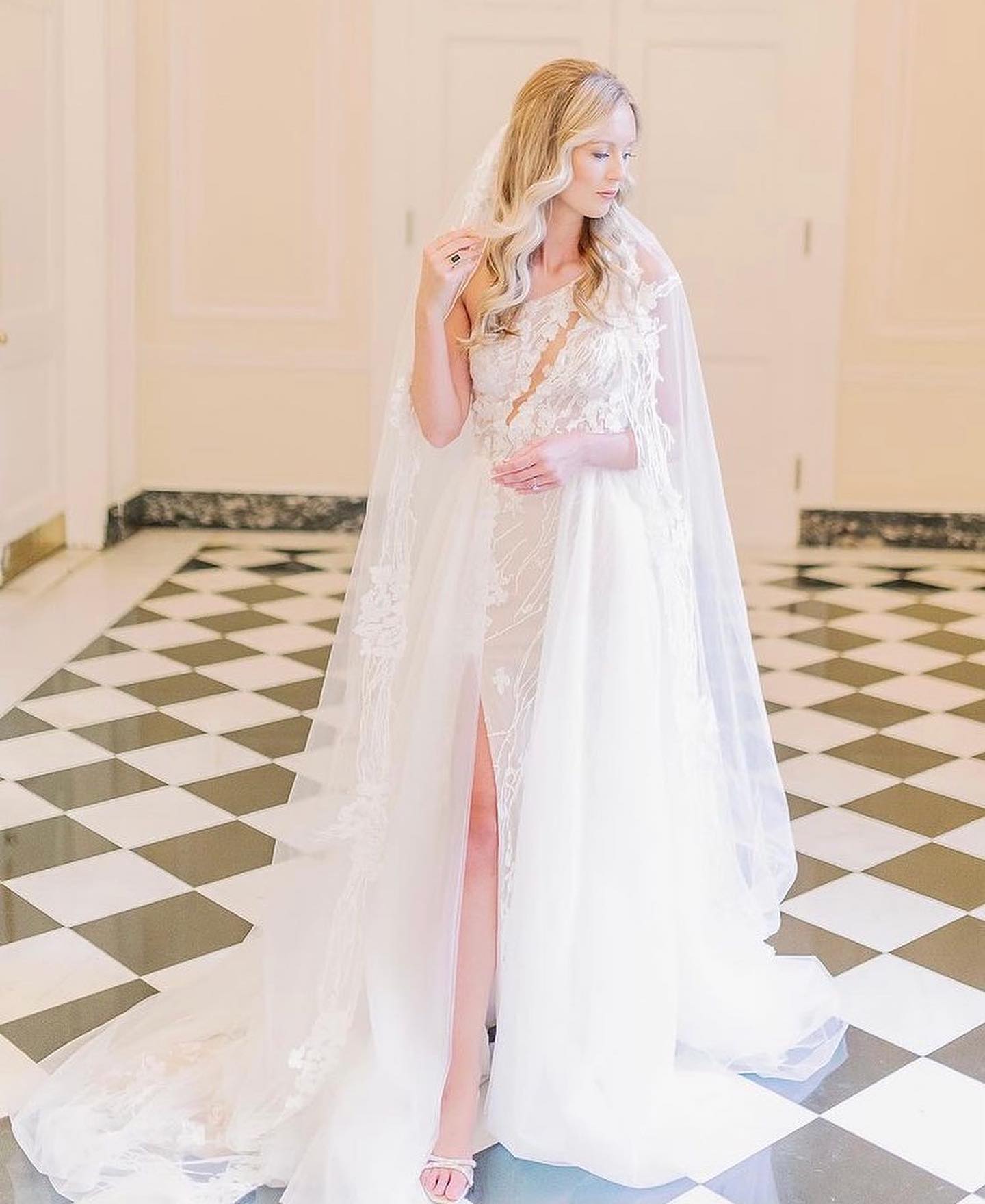 A woman in a wedding dress and veil is standing on a checkered floor.