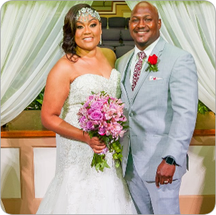 A bride and groom pose for a picture while the bride is holding a bouquet of pink flowers