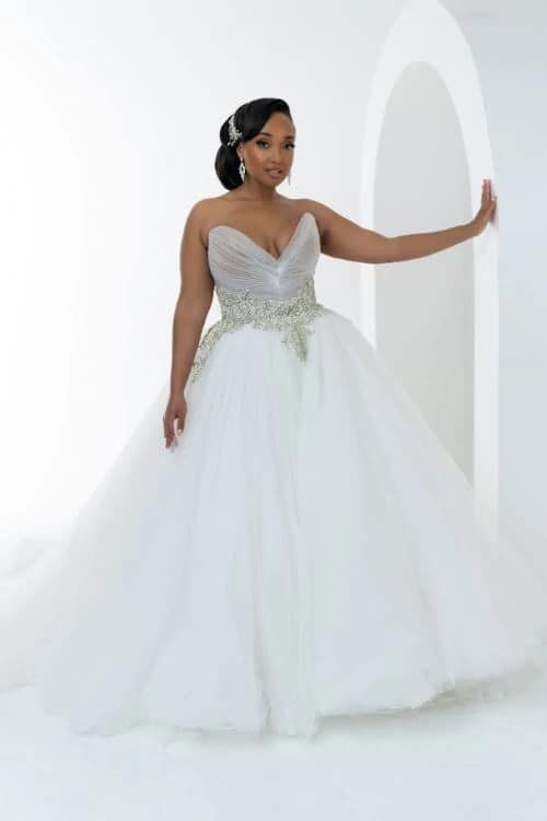 A woman in a white ball gown is standing in front of a white wall.