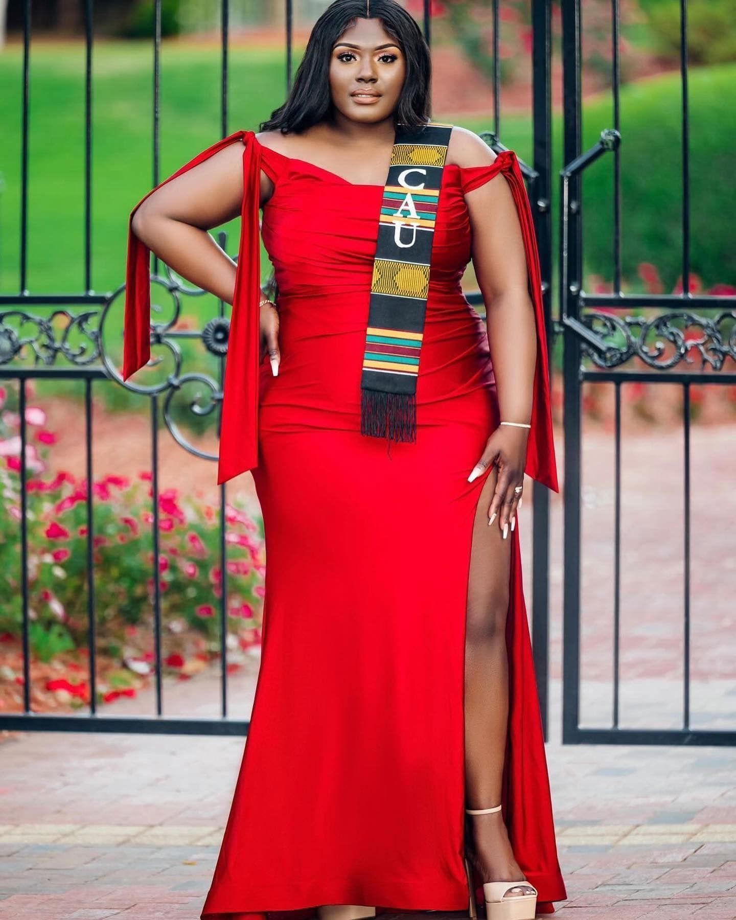 A woman in a red dress is standing in front of a gate.