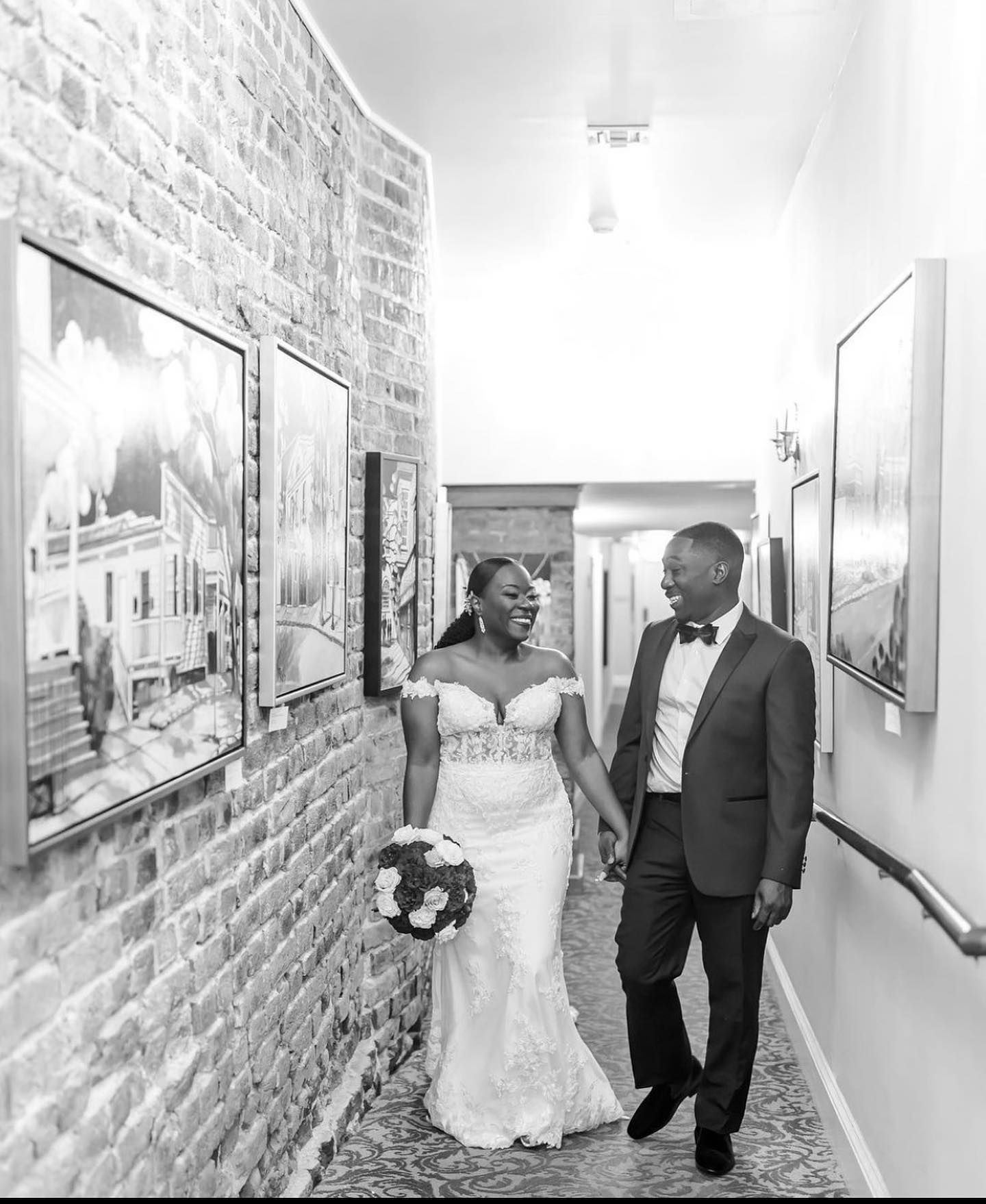 A bride and groom are walking down a hallway holding hands.