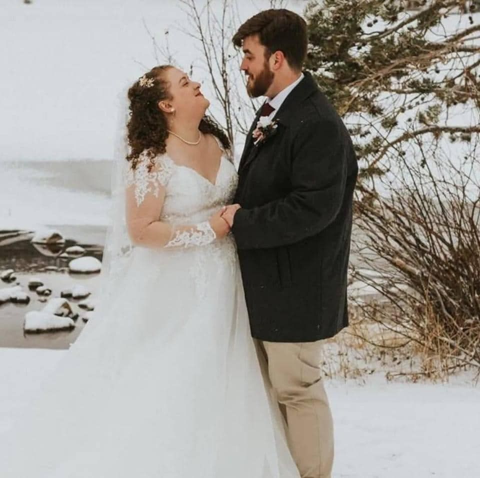 A bride and groom are posing for a picture in the snow.