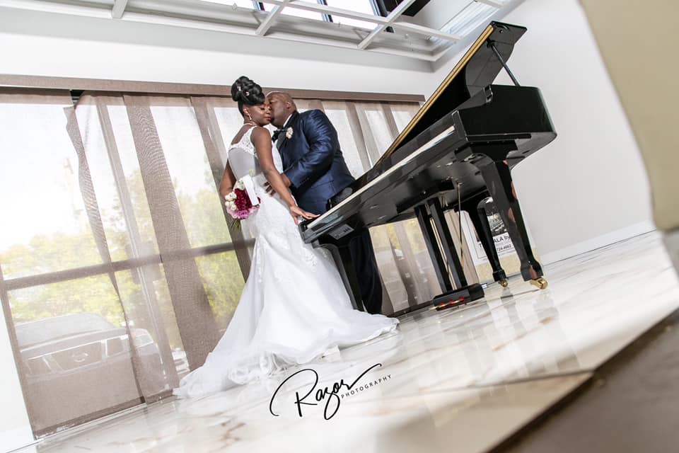 A bride and groom are kissing in front of a piano.