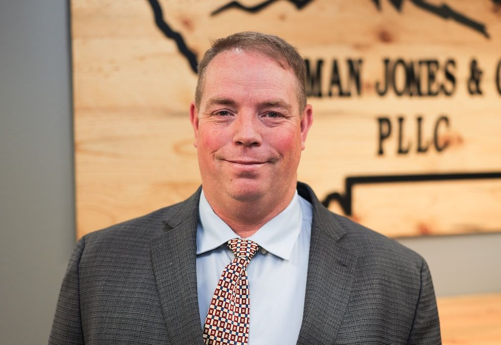 Man in suit smiles in front of a wood-paneled wall with a company logo.