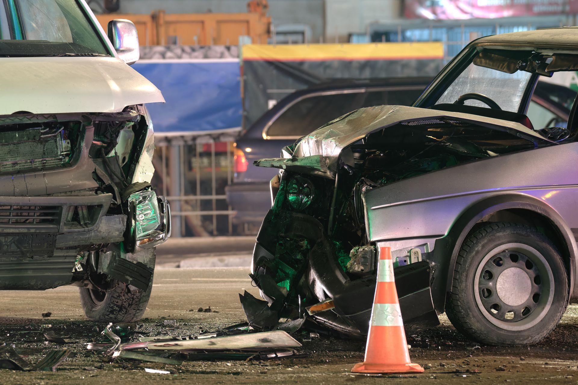 Two vehicles with severe front-end damage after a collision, with an orange traffic cone in the foreground.