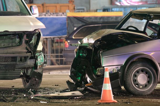 Two vehicles with severe front-end damage after a collision, with an orange traffic cone in the foreground.