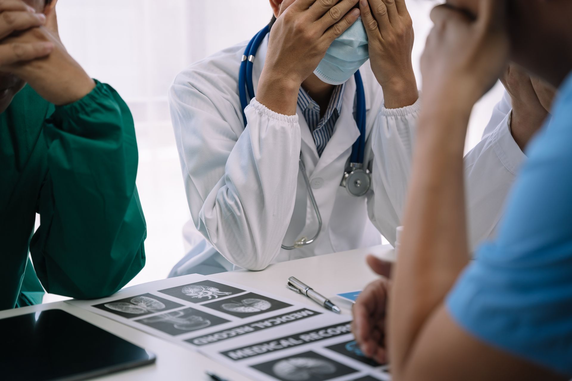 Doctors in distress, heads in hands, at a table with medical scans.