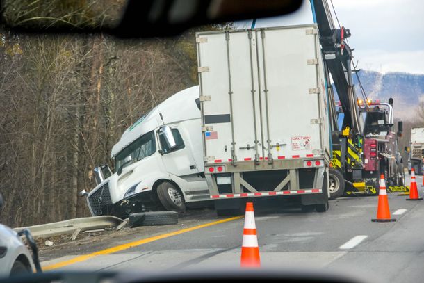 Semi-truck crashed on side of highway, being towed by a wrecker.