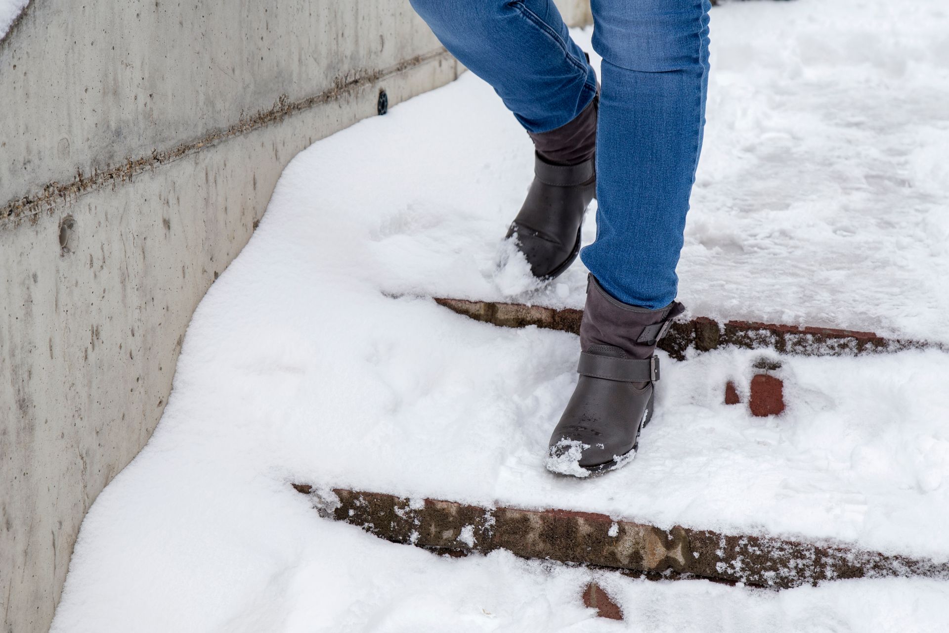 Person wearing boots and jeans walking down snow-covered concrete steps.