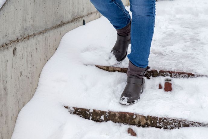 Person wearing boots and jeans walking down snow-covered concrete steps.