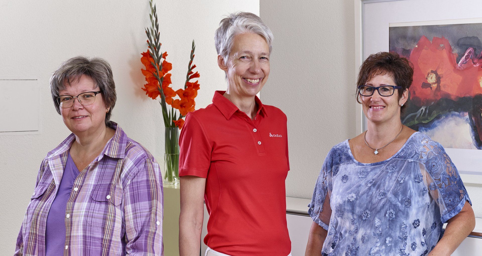 Drei Frauen stehen nebeneinander in einem Raum und lächeln.