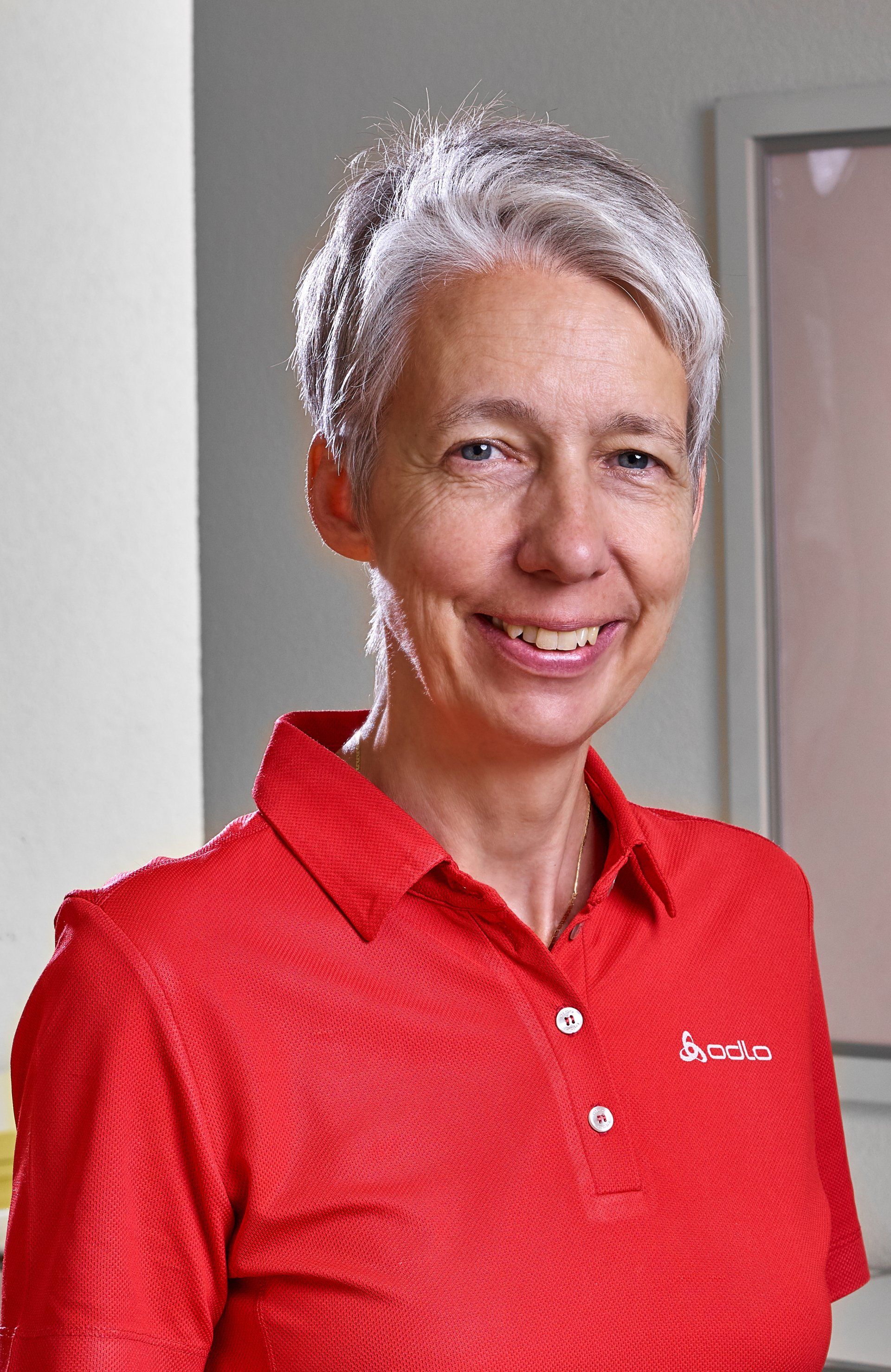 Eine Frau mit grauem Haar trägt ein rotes Hemd und lächelt.