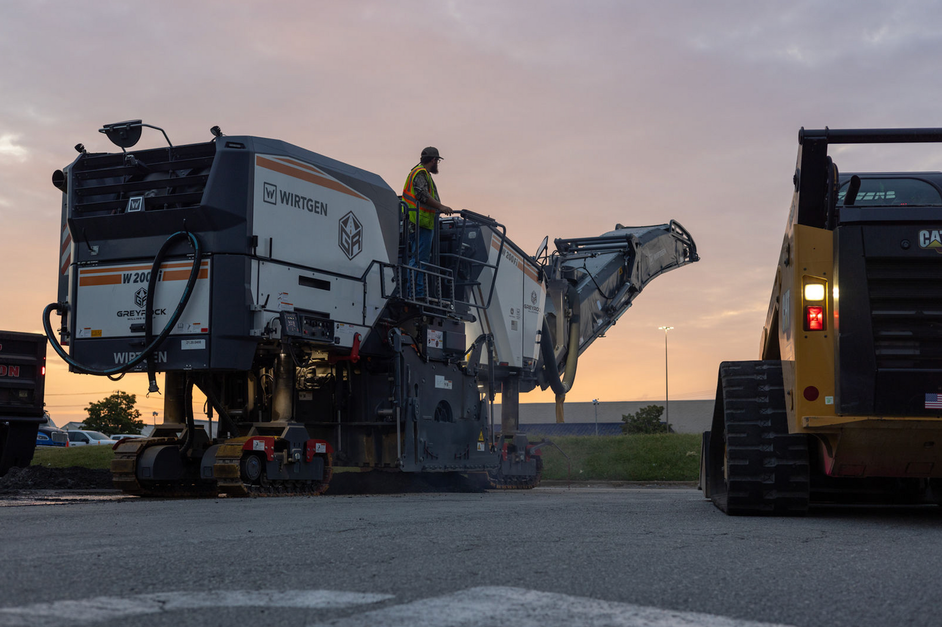 A man is standing on top of a large machine in a parking lot.